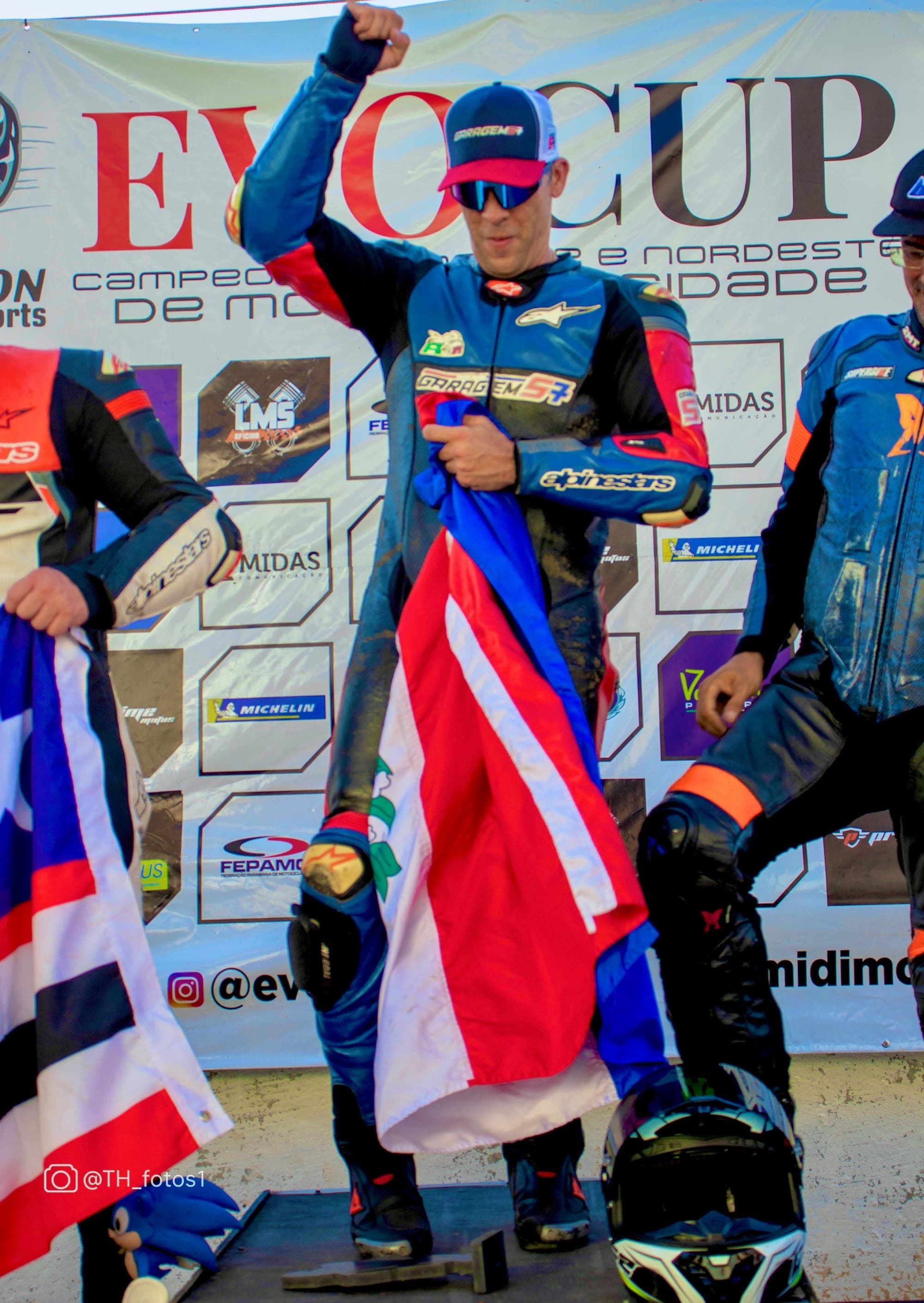 Hilton no pódio do EVO CUP com o punho erguido segurando bandeira
